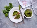 Pesto ze szpinaku do słoików na chlebie z pestkami słonecznika. Świeży szpinak obok talerza.