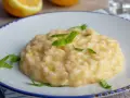 Kremowe, letnie risotto z cytryną i bazylią, podane na białym talerzu z niebieskim rantem.