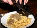 Dłonie trą całe grzyby trufle nad talerzem tagliatelle.