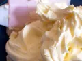 Puszysty, prosty krem z mascarpone bez śmietany, idealny do deserów. Widać go na niebieskim tle, obok różowej łopatki.
