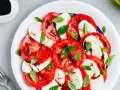 Pyszna sałatka caprese z pomidorów, mozzarelli i bazylii, polana sosem balsamicznym.