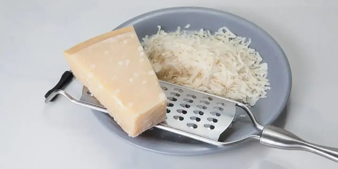Kawałek parmezanu i starty ser na talerzu. Zastanawiasz się, czy parmezan można mrozić? Tak, można go mrozić, zachowuje wtedy smak.