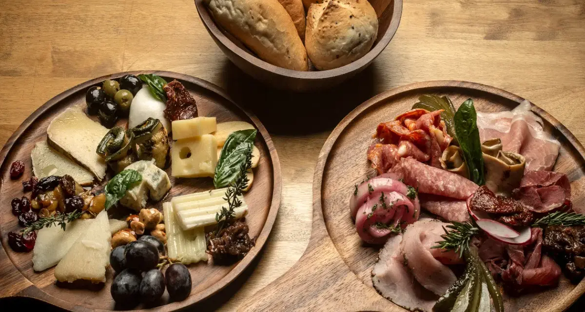 Deska serów i wędlin inspiracje: bogactwo smaków i aromatów na drewnianych deskach, z pieczywem w tle.