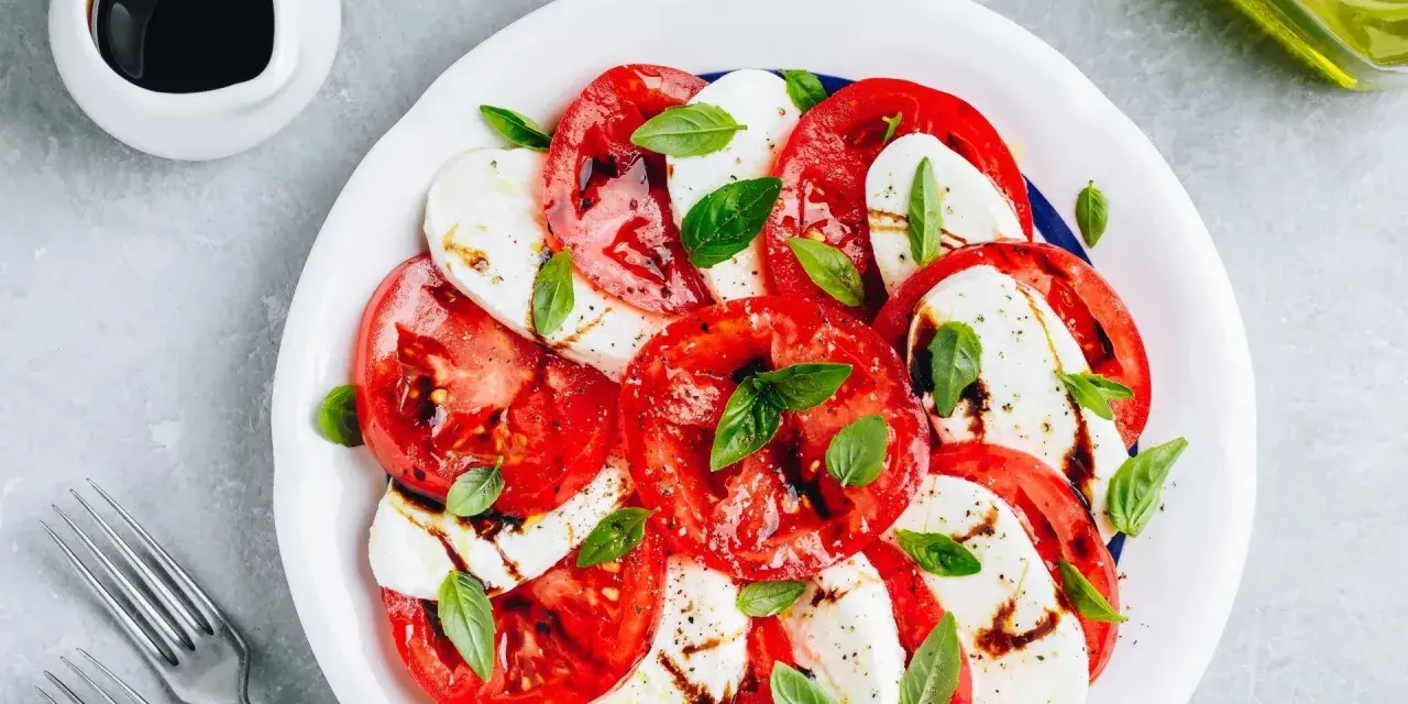 Pyszna sałatka caprese z pomidorów, mozzarelli i bazylii, polana sosem balsamicznym.
