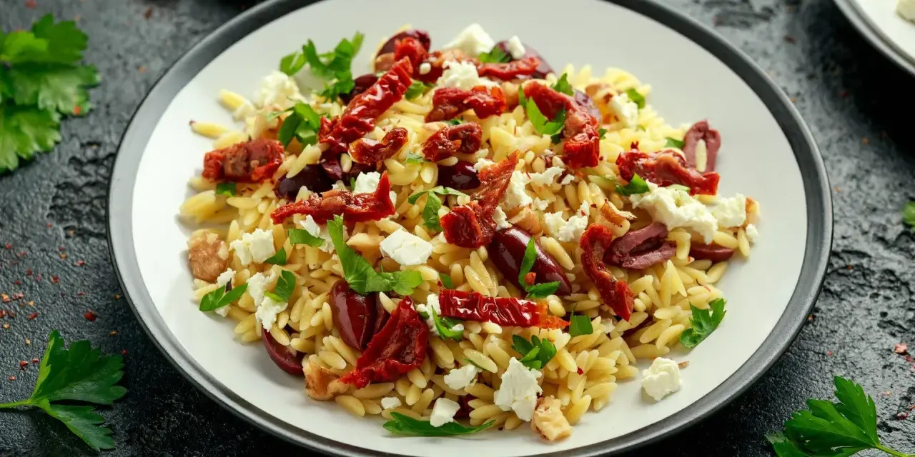 Pyszna sałatka z makaronem orzo, z suszonymi pomidorami, oliwkami, fetą i natką pietruszki. Idealna na lekki posiłek.