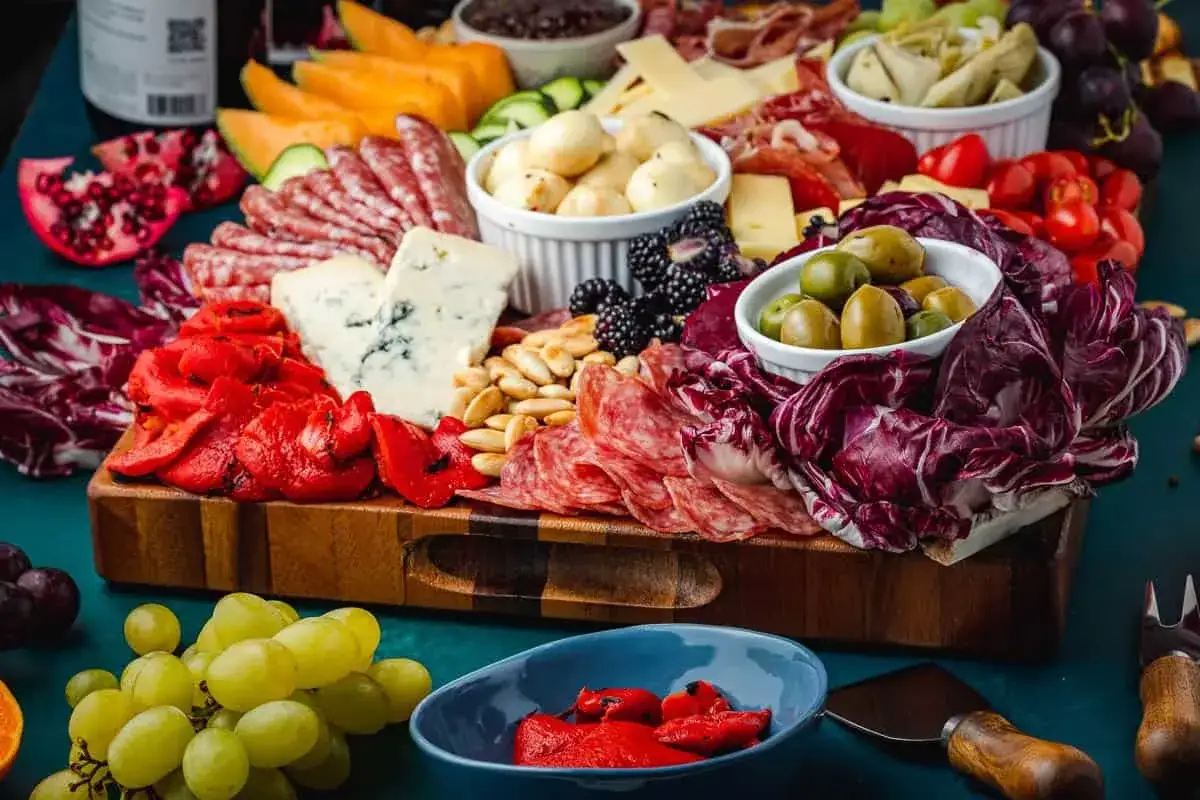 Deska serów i wędlin inspiracje: bogactwo smaków i kolorów. Salami, sery pleśniowe, oliwki, owoce i warzywa tworzą apetyczną kompozycję.