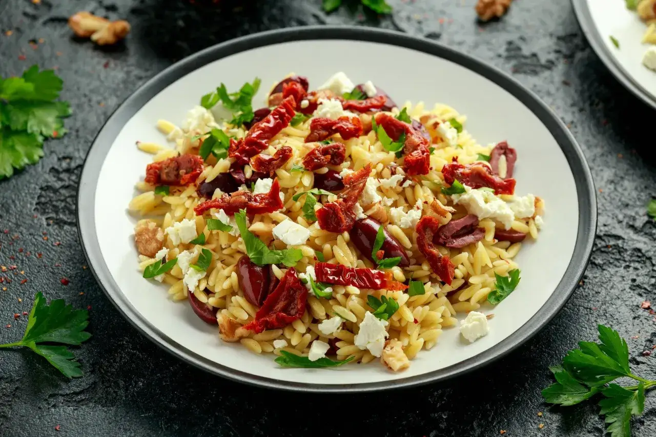 Pyszna sałatka z makaronem orzo, z suszonymi pomidorami, oliwkami, fetą i natką pietruszki. Idealna na lekki posiłek.