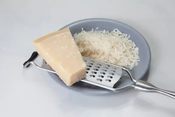 Kawałek parmezanu i starty ser na talerzu. Zastanawiasz się, czy parmezan można mrozić? Tak, można go mrozić, zachowuje wtedy smak.
