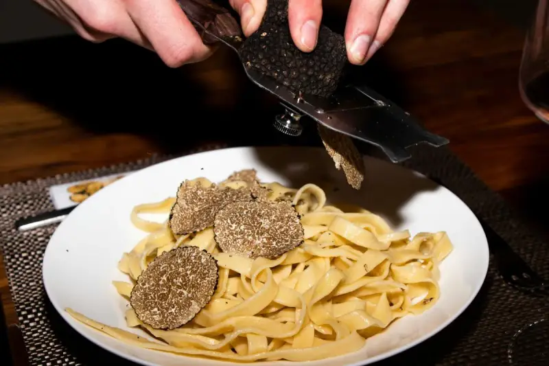 Dłonie trą całe grzyby trufle nad talerzem tagliatelle.