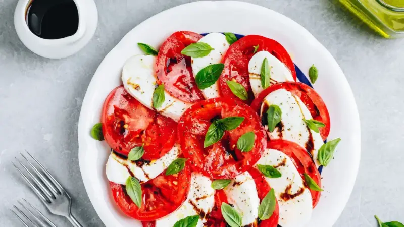 Pyszna sałatka caprese z pomidorów, mozzarelli i bazylii, polana sosem balsamicznym.